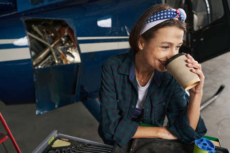 Joyful woman relief engineer in uniform resting during the break in hangarの写真素材