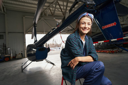 Beautiful smiling brunette airframe engineer sitting in the aviation garageの写真素材