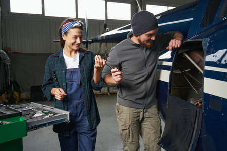 Charming male and female wearing uniform repairing the motor in aviation garageの写真素材