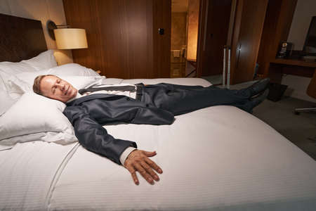 Relieved-looking enterpreneur relaxing in bed after exhausting tripの写真素材