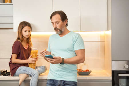 Adult man and teen girl together in the kitchen with a smartphone and pasta