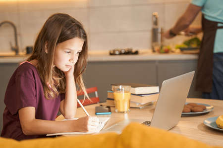 Teenager is working on a computer at the kitchen tableの写真素材