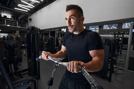 Delighted male person building muscles on arms