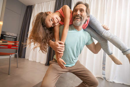 Adult man playing crouches with a teenager around his neckの写真素材