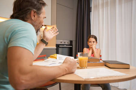 Girl sitting at the kitchen table in front of angry manの写真素材