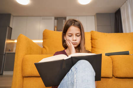 Teenager is sitting with an open book and reading it