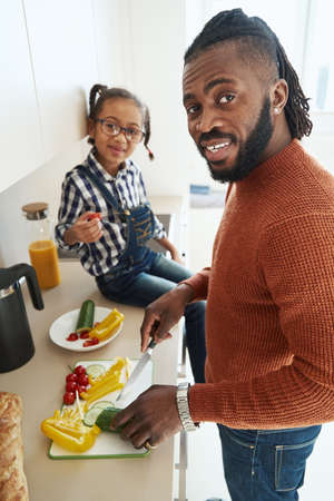 Joyful African American man enjoying cooking with his daughter