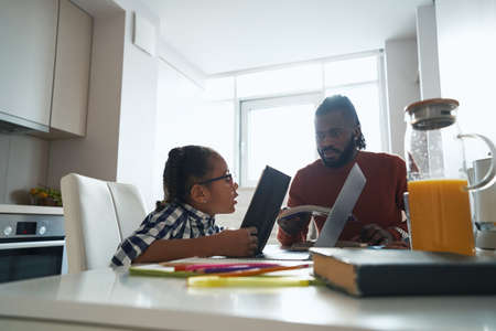 African American man listening intently his young daughter who reading bookの写真素材