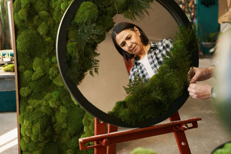 Woman gluing green plant on round mirrorの写真素材