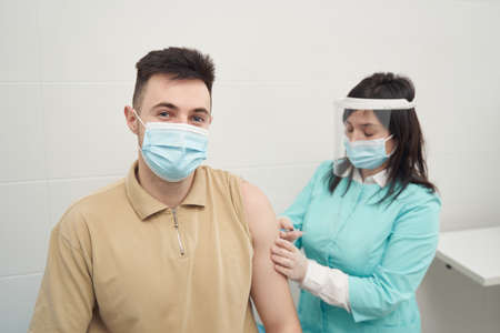 Young man being vaccinated by woman in clinicの写真素材