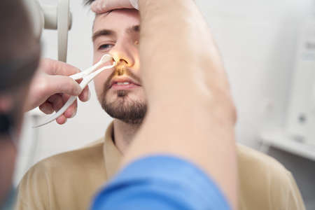 Male otorhinolaryngolosist examining young man in clinic