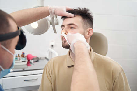 Cheerful young man being examined otorhinolaryngolosist in officeの写真素材