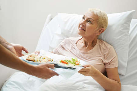 Aging lady getting meal tray from hospital employeeの写真素材