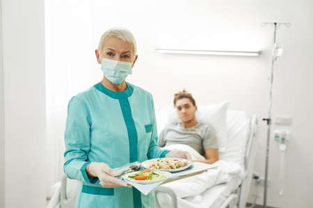 Elderly nurse standing with tray of foodの写真素材