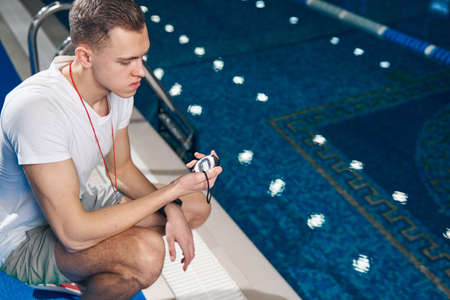 Young caucasian guy checking the time in the timer near the swimming poolの写真素材
