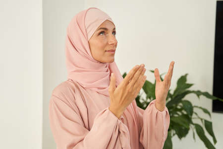 Islamic young woman in hijab praying while looking up in the room