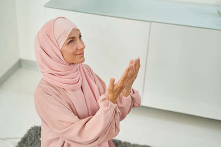 Smiling young Muslim woman praying glorifying God at home