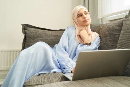 Muslim woman sitting on couch with laptop at home