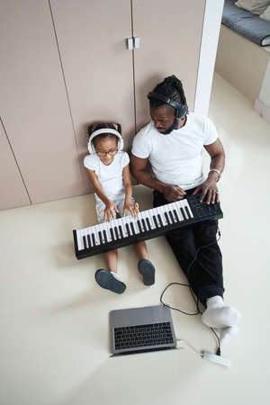 Adult African American father next to daughter plays the synthesizerの写真素材