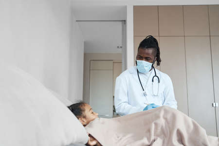 Lying in bed African American girl listens to an adult doctorの写真素材
