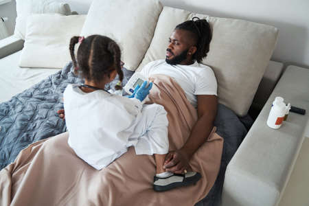 African American girl examines medical device on a lying father