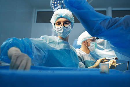 Female surgery assistant taking another instrument from tray