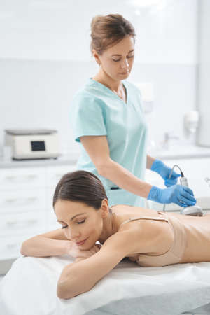 Focused beautician conducting radiofrequency skin rejuvenation on back