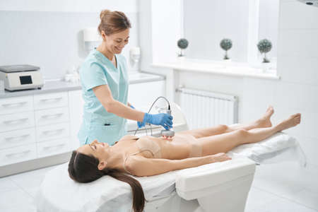 Happy woman beautician carrying out radiofrequency lifting of stomach