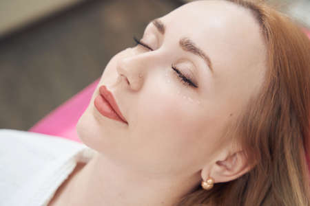 Happy cheerful female is getting anti-aging facial skin care in beauty center