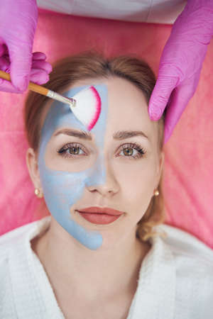 Happy cheerful young female is getting skin care with mask in beauty center