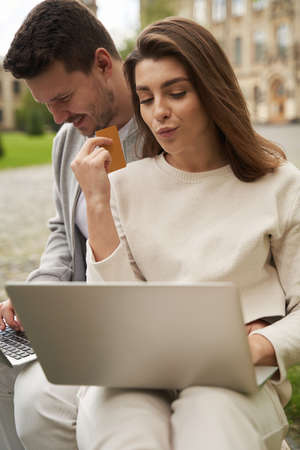Happy couple using laptops for online shopping outdoors