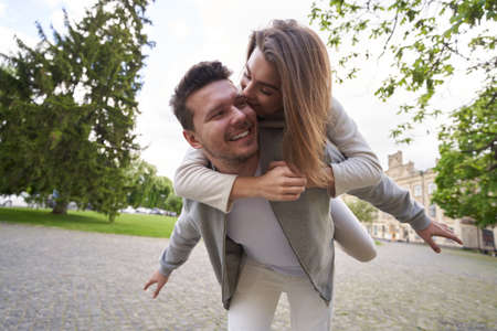 Happy man in love carrying woman on his back outdoors