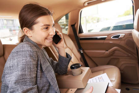Cheerful businesswoman talking on mobile phone in car