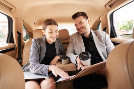 Cheerful man and woman working on business project in car