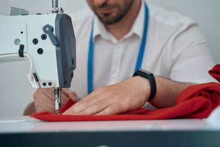 Smiling tailor with smartwatch using sewing machine