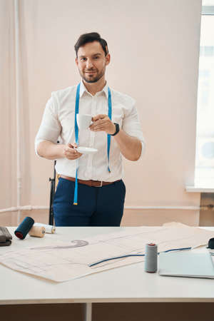 Young fashion designer drinking coffee in own tailor office