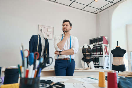 Man couturier in shirt thought among the sewing workshopの写真素材