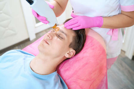 Young man during epilation in cosmetologist officeの写真素材