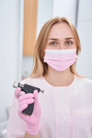 Doctor is in cabinet holding a professional device for piercing