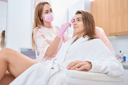 Doctor performs a cosmetic procedure on face of young patientの写真素材