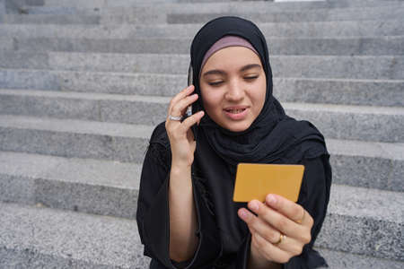 Muslim woman talking on the phone holding a business cardの写真素材