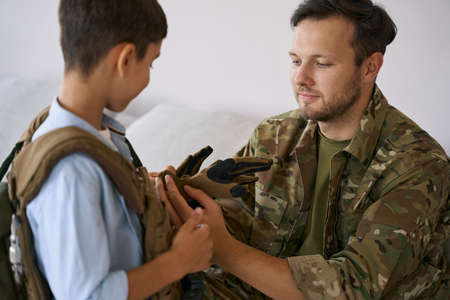 Serviceman dressing his son in military clothes
