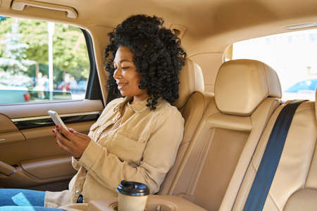 Passenger in back seat with phone and glass of coffee