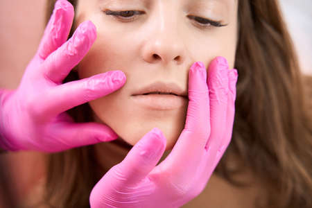 Female face is examined by medical worker with both hands