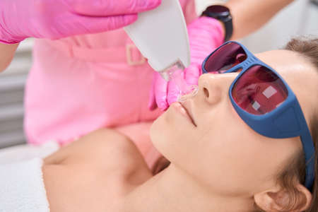 Aesthetic medicine doctor holding laser epilator on a female faceの写真素材