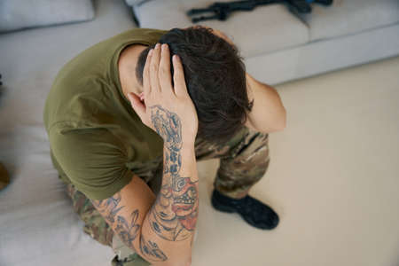 Man of arms experiencing mental problems and holding his headの写真素材