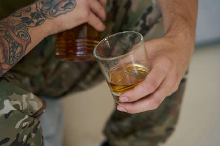 Glass of whisky in hand of drinking military manの写真素材