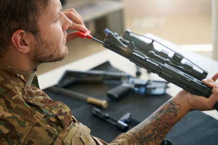 Military man is cleaning his disassembled firearm