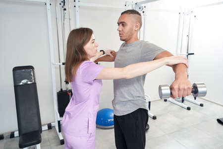 Female physiotherapist helping man to perform rehabilitation exerciseの写真素材