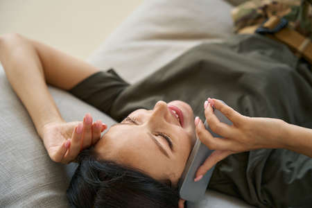 Woman soldier resting on sofa and talking on mobile phone